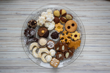 Many kinds of Christmas cookies on cut glass transparent plate, sweet food on wooden table