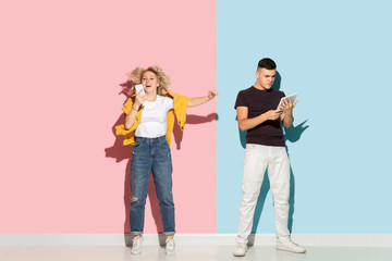 Fototapeta premium Young emotional man and woman in bright casual clothes posing on pink and blue background. Concept of human emotions, facial expession, relations, ad. Man's sad, woman's astonished, crazy happy.