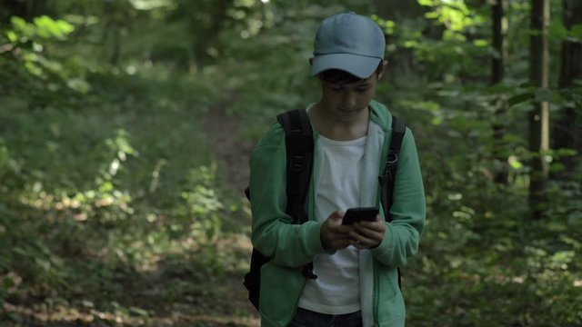 boy walking in the forest and uses a phone outdoors