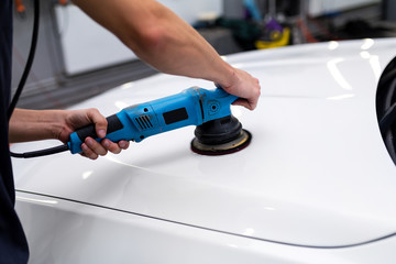 A man polishes the painted surface of a car with a pneumatic polishing machine.