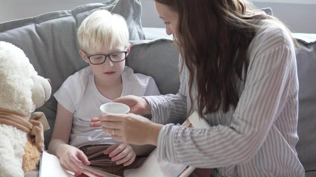 Mom gives the child a medicine and a glass of water to drink a pill. Mom gives her son vitamin D and a glass of water.