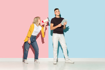 Obraz premium Young emotional man and woman in bright casual clothes posing on pink and blue background. Concept of human emotions, facial expession, relations, ad. Man's ignoring woman with mouthpeace.