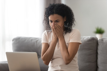 Fototapeta na wymiar Stressed biracial woman shocked by unbelievable laptop message