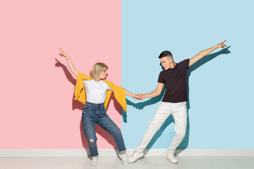 Naklejka premium Young emotional man and woman in bright casual clothes posing on pink and blue background. Concept of human emotions, facial expession, relations, ad. Beautiful caucasian couple dancing together.