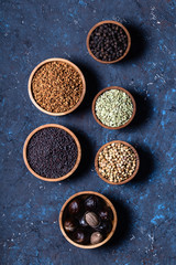 Dry whole Indian spices in wooden bowls on dark blue concrete rustic background.