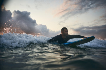 Male surfer getting ready for ride on the ocean wave against beautifull sinset light
