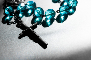 Rosary with cross and blue beads isolated on silver background with copy space. Christian religion and faith symbol background.