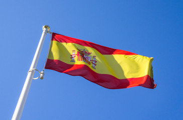 Spanish flag waving in the wind against a blue sky.