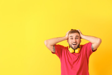Fototapeta na wymiar Surprised young man with headphones on color background