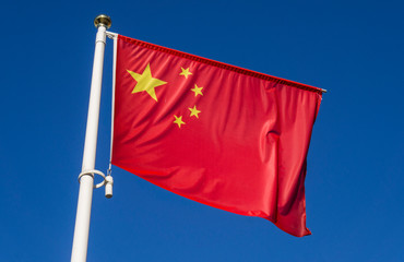Chinese flag waving in the wind against a blue sky.