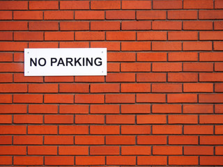 Fototapeta na wymiar a white sign saying no parking on a red brick wall