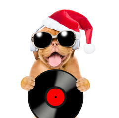 Happy puppy wearing a sunglasses and red santa hat listen music with headphones and holds vinyl record. Isolated on white background