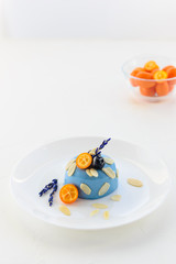 Panna cotta dessert with blue matcha, kumquat, blueberries and lavender on a white plate.