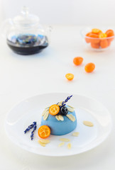 Panna cotta dessert with blue matcha, kumquat, blueberries and lavender on a white plate.