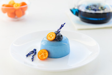 Panna cotta dessert with blue matcha, kumquat, blueberries and lavender on a white plate.