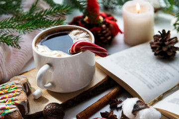 mug of hot black coffee with marshmallow and Lollipop, candle, cookies, open book, cone,