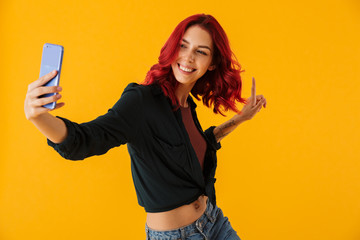Image of smiling woman pointing finger upward and taking selfie photo