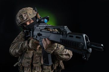 Fototapeta premium a male soldier in military clothes with a weapon on a dark background