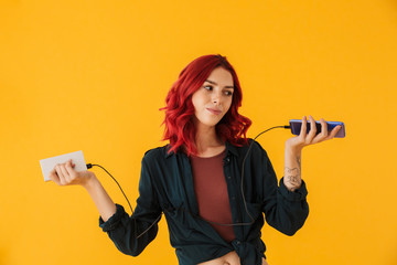 Image of nice puzzled woman holding cellphone and power bank