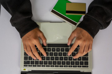 The hacker is using a notebook and has a gold credit card and a bank account placed on a white table.