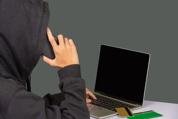 The hacker is sitting on the phone on his notebook and has a gray background.