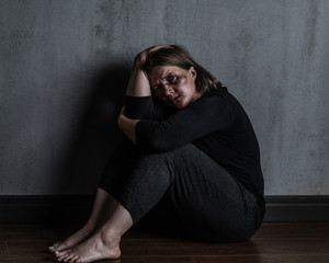 Sad woman victim of domestic violence and abuse sits on a floor at home