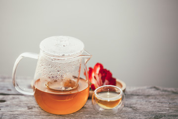 The hot tea contained in the pitcher is placed beside the glass of tea on a wooden floor above water.