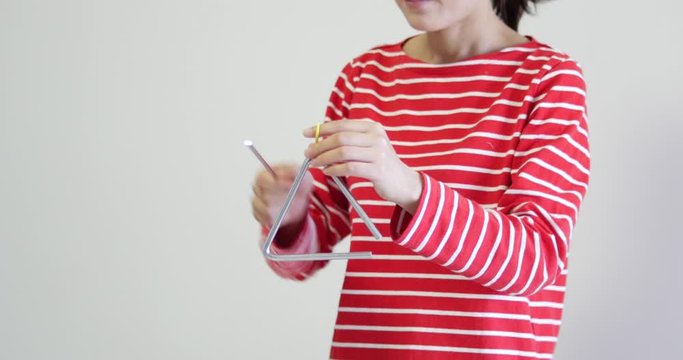 Unrecognizable woman wearing red and white striped clothes playing the triangle. a percussion instrument often used in orchestras and in music schools for art education