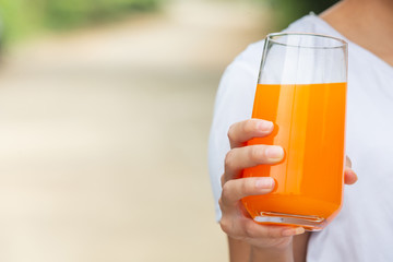 A beautiful woman wearing a white T-shirt holding a glass of orange juice and having a green nature background.