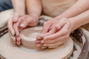 Fototapeta na wymiar Potter teaches woman to make ceramic pot on the pottery wheel