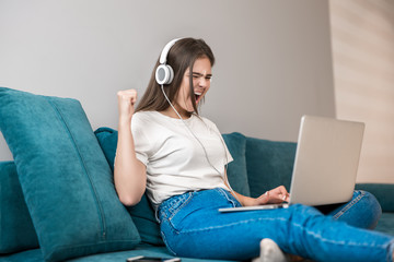 young beautiful sucessful woman in headphones working in her laptop on the sofa in the living room looking very happy