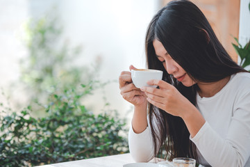 A beautiful woman wearing a long-sleeved white shirt sitting at a coffee shop.