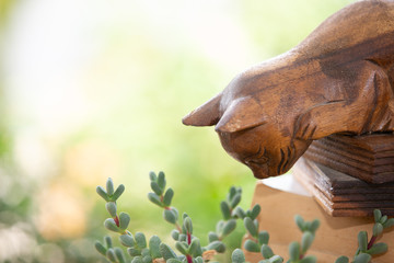 A carved wooden cat was staring at the top of the flower below and had a blurred background.