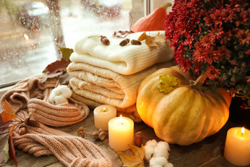 Beautiful autumn composition with pumpkin, warm clothes and candles on window sill