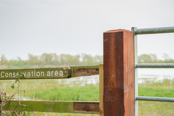 Close-up view of a wooden conservation area sign seen attached near a gated entrance. The reserve...