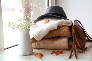 Stack of warm clothes with flowers on window sill