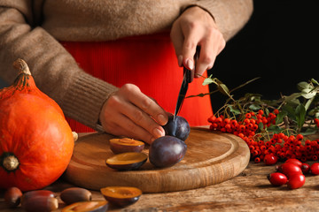 Woman cutting fresh plums at wooden table