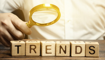 Wooden blocks with the word Trends and businessman with a magnifying glass. Popular and relevant...