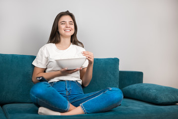Obraz premium beautiful young woman watching funny movie on the sofa eating popcorn feeling comfortable on the sofa at home laughing