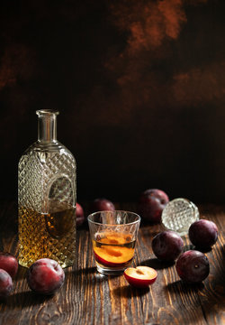 Rakia or rakija traditional Balkan fruit brandy. Plum brandy sljivovica in a glass and decanter on a wooden table and dark background. Vertical. Copyspace