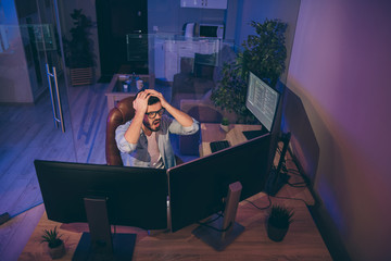 Oh no. Hign angle view photo of it specialist loser guy sitting chair many monitors noticed server debugging holding hands on head need to edit errors night office indoors