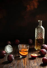 Rakia or rakija traditional Balkan fruit brandy. Plum brandy sljivovica in a glass and decanter on a wooden table and dark background. Vertical. Copyspace