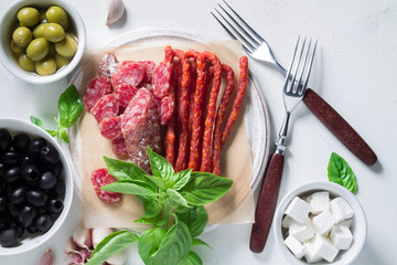 Set of chorizo sausages with olives and a sprig of basil. Antipasti snack.