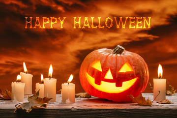 Halloween luminous jack-o-lantern pumpkin, autumn leaves and burning candles on wooden background....