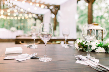 Rustic table setting with floral decorations, lanterns. Wineglasses on the table. Wedding or dinner table in restaurant outdoors