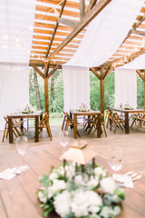 Wedding tables in restaurant outdoors. Banquet. The chairs and table for guests, decorated with lanterns and flowers, served with cutlery and crockery. Restaurant outdoors in forest or garden