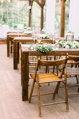 Fototapeta na wymiar Wedding tables in restaurant outdoors. Banquet. The chairs and table for guests, decorated with lanterns and flowers, served with cutlery and crockery. Restaurant outdoors in forest or garden