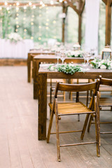 Wedding tables in restaurant outdoors. Banquet. The chairs and table for guests, decorated with lanterns and flowers, served with cutlery and crockery. Restaurant outdoors in forest or garden