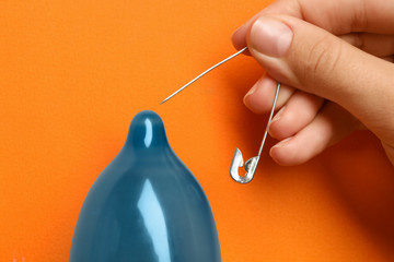 Woman piercing inflated condom with pin on orange background, closeup. Safe sex