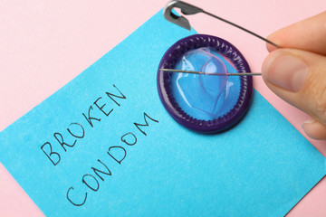 Woman piercing condom with pin on pink background, closeup. Safe sex